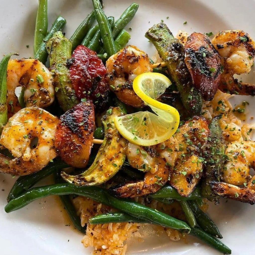 Savor grilled shrimp and vegetables, including green beans and okra, garnished with herbs and lemon slices over seasoned rice—a taste of Acworth Travel's local culinary delights.