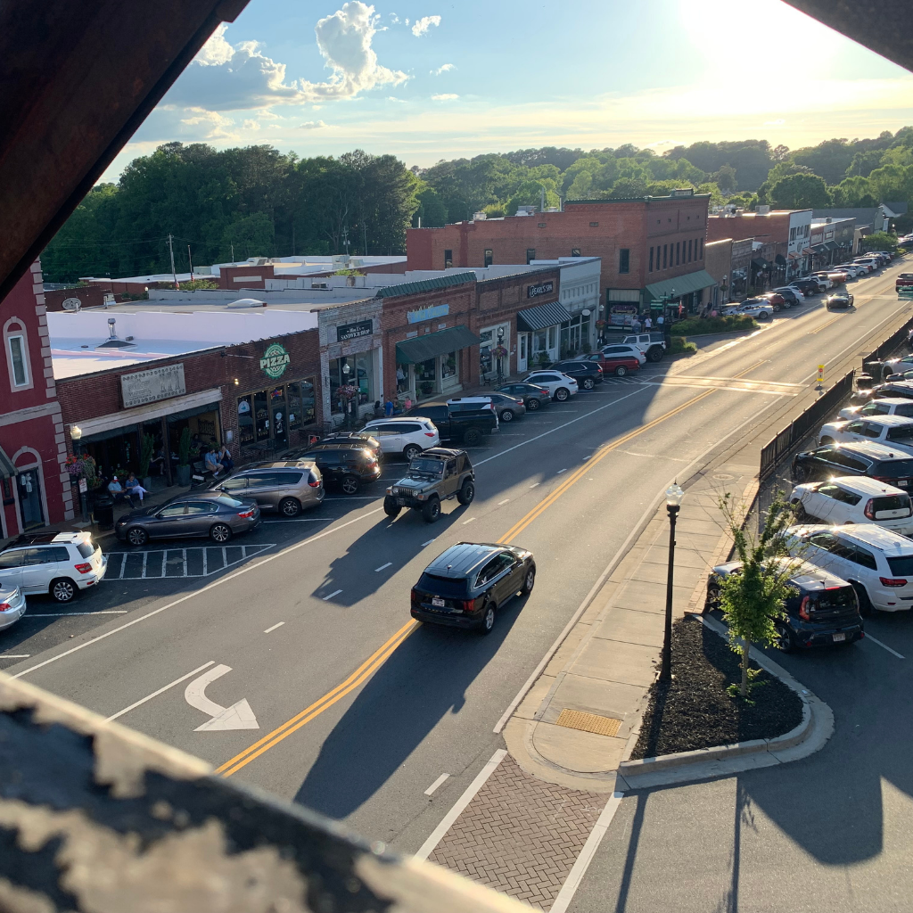 A street scene in Acworth Travel shows cars parked along storefronts and trees in the background, taken from an elevated vantage point in the late afternoon.