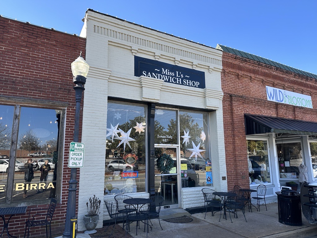 Facade of a sandwich shop with glass windows, Christmas decorations, and outdoor seating. A sign reads 