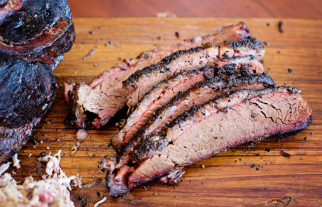 Sliced smoked brisket on a wooden cutting board, showcasing a seasoned crust and tender interior with a visible smoke ring.