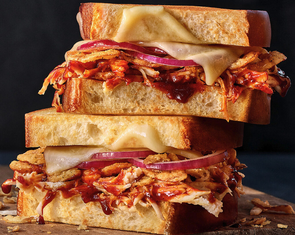 Stacked grilled cheese sandwiches with pulled chicken, cheese, barbecue sauce, and onion slices on toasted bread.