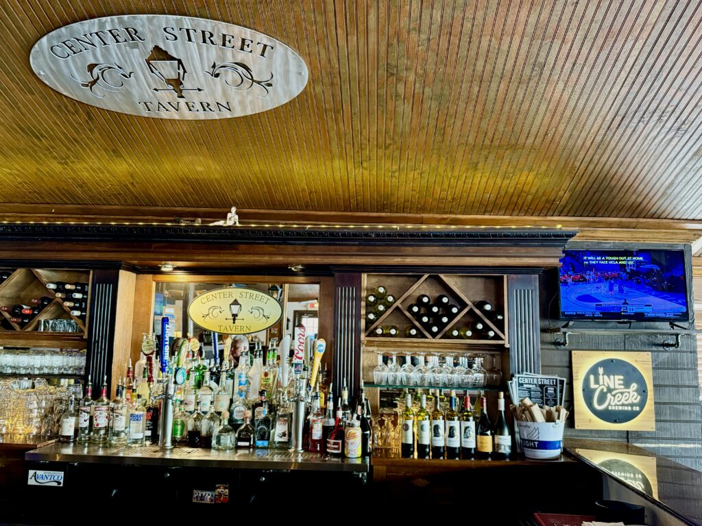 Bar interior with a variety of liquor bottles on display, a centered logo sign reading 