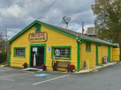 Yellow and green building with a sign reading "Rico's Mex Mex Grill." It has a satellite dish on the roof and a small bench outside.