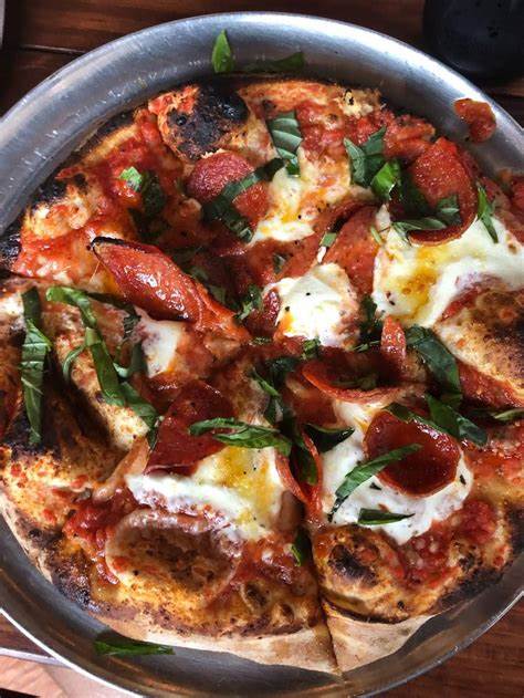 A pizza topped with pepperoni, mozzarella cheese, tomato sauce, and fresh basil, served on a metal tray.