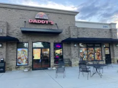 Brick storefront of a restaurant called Daddy's, with outdoor tables and chairs, large menu posters on windows, and a lit open sign by the entrance.