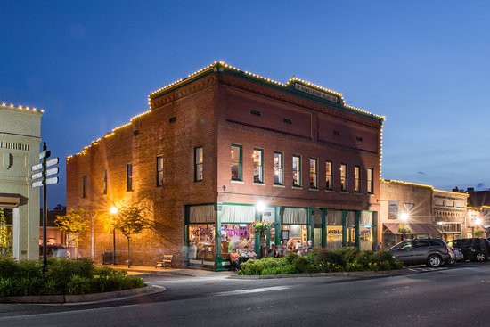 Historic brick building with lit outline at dusk, street corner, windows lit, parked cars, and street signs visible.