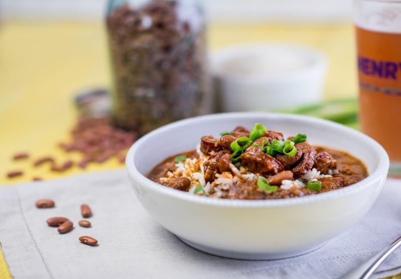 A bowl of chili with beans and rice, topped with green onions. A jar of beans and a glass are in the background.