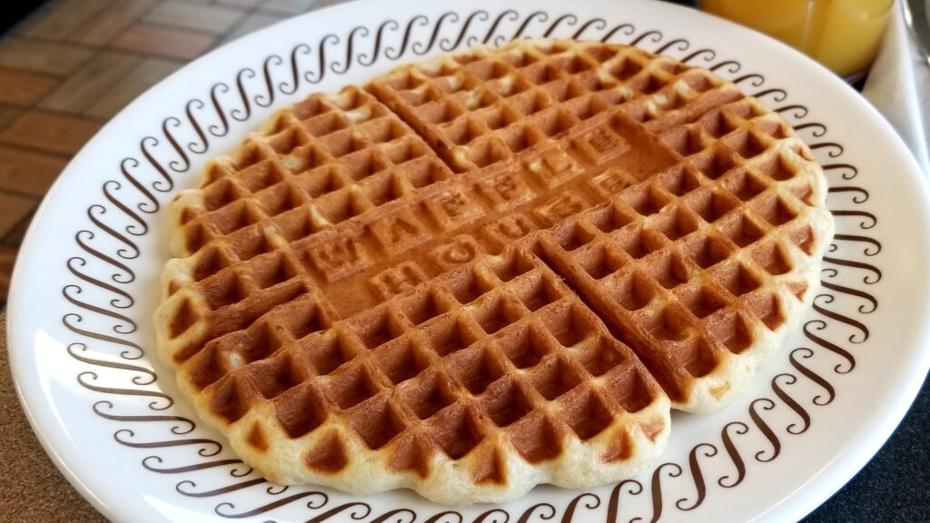 A round, golden-brown waffle on a decorative plate.