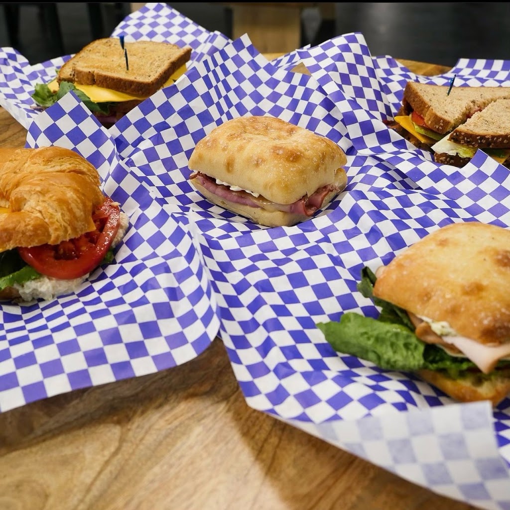 An assortment of sandwiches on blue and white checkered paper, including a croissant and ciabatta bread, displayed on a wooden surface.