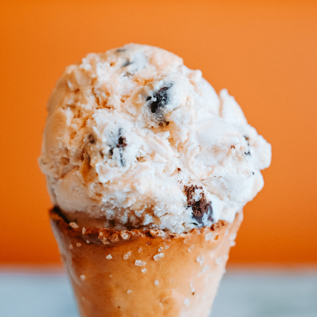 Ice cream cone with a scoop of cookies and cream ice cream against an orange background.