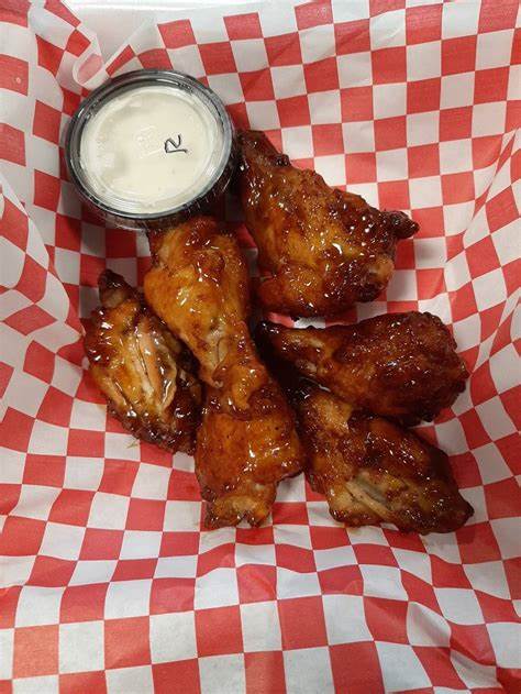 Six glazed chicken wings and a small container of ranch dressing in a red and white checkered paper tray.