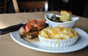 Foodies and fun-seekers flock to Acworth for a plate with grilled meat topped with cooked apples, baked macaroni and cheese, and a bowl of greens with a piece of cornbread.