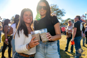 Two women with drinks smiling on a sunny day at the park