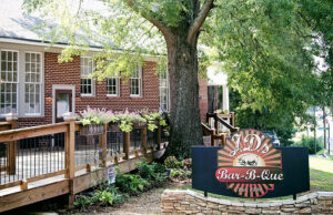 Foodies and fun-seekers flock to Acworth for a taste of AJ's Bar-B-Que, a restaurant established in 1999. Tucked inside a charming brick building with a wooden ramp, it's marked by a delightful sign under a large tree.