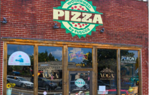 Exterior of Fuscos Pizza, a brick building with large windows displaying signs for pizza, gelato, and beer. The "Pizza" sign at the top indicates woodfired pizza—a hotspot where foodies and fun-seekers flock to Acworth.