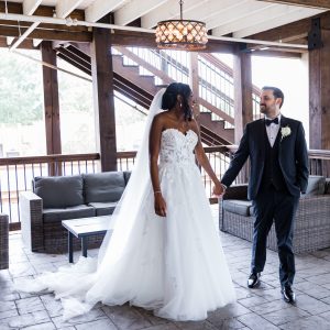 A bride in a white gown and a groom in a black tuxedo stand indoors on a patio, holding hands and looking at each other—Celebrate Your Event in Acworth!.