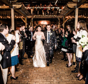 A bride and groom walk through a crowd of cheering guests under string lights, with bubbles floating around, as foodies and fun-seekers flock to Acworth for the celebration.