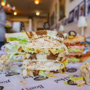 A stacked sandwich with turkey, lettuce, and cheese sits invitingly on a deli counter in Acworth, while pasta salad adds a tasty side temptation. Five New Reasons to put Acworth on your Travel Bucket List include its delicious culinary treats like this.