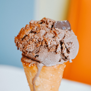 A scoop of chocolate ice cream on a cone, topped with chocolate chunks, tempts taste buds against a colorful backdrop—just one of five new reasons to put Acworth on your travel bucket list.