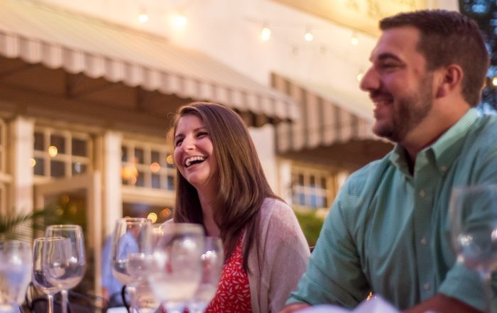 Two people sit at an outdoor restaurant table, smiling and laughing under string lights. Discover moments like this at one of the 6 MUST-VISIT SPOTS FOR THE PERFECT VALENTINES DAY IN ACWORTH.