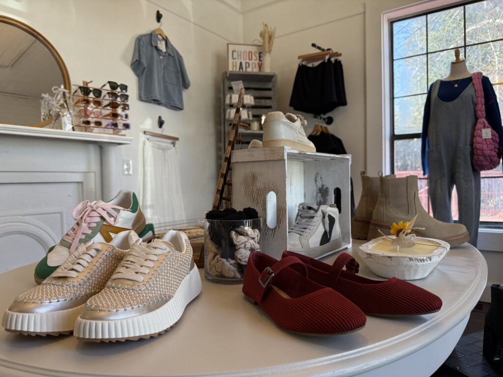 Display of various shoes, shirts, sunglasses, and accessories on a round table in a clothing store, with more items and a 