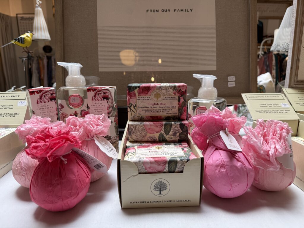 A display of pink-wrapped bath products and soaps with floral designs, including boxed soaps labeled 