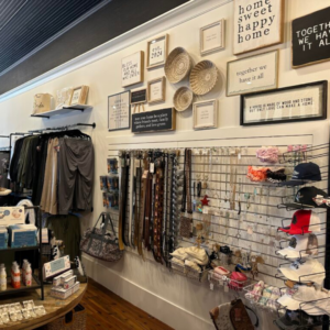 The charming boutique shop in Acworth showcases clothing, bags, jewelry, and home decor. Framed quotes and woven baskets add a cozy touch above the merchandise, creating an inviting atmosphere perfect for exploring winter combos that lift your mood.