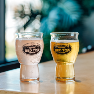 Two beverages in glasses with the "Red Top Brewhouse" logo sit invitingly on a table: one clear and bubbly, the other golden. Perfect pairings to savor during your visit for 6 Winter Combos for Fresh Food + a Good Mood in Acworth.