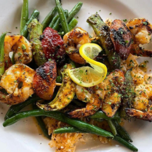 A plate of grilled shrimp and vegetables is perfectly garnished with lemon slices and herbs, served over green beans—one of the delightful winter combos for fresh food that promises a good mood in Acworth.