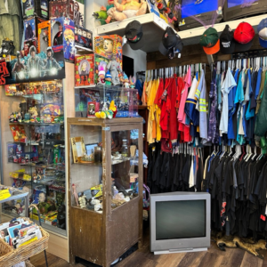 A vintage store in Acworth brimming with collectibles, racks of clothing, and quirky hats. Nestled amidst the treasures is a CRT television on the floor, setting a nostalgic vibe reminiscent of winter combos that bring both fresh finds and a good mood.