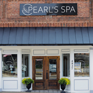 Front view of Pearl's Spa with a brick facade, black awning, and wooden double doors. The entrance is flanked by windows and two potted plants, making it a serene retreat. Signage displays the spa's name above the door—one of Acworth's 6 must-visit spots for the perfect Valentine's Day.