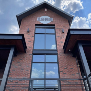 Brick building with a large window and "1885" displayed near the roofline, reminiscent of Acworth's charming history. Metal railing in the foreground. The sky offers scattered clouds, perfect for enjoying 6 winter combos for fresh food and a good mood in this delightful setting.