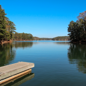 A wooden dock extends over a calm lake surrounded by trees under a clear blue sky, inviting you to discover five new reasons to put Acworth on your travel bucket list.