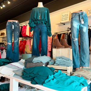 In a chic Acworth boutique, discover 6 winter combos for fresh style: mannequins in teal tops and jeans stand among folded clothes and ankle boots, all setting the stage for fashion that uplifts your mood this season.