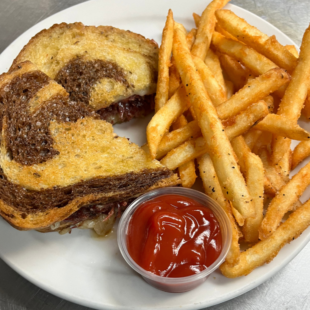 A sandwich layered with brown and white bread, paired with seasoned fries and a small cup of ketchup on a white plate, is among our favorite winter combos for fresh food and a good mood in Acworth.