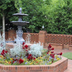 Amid the 6 must-visit spots for the perfect Valentine's Day in Acworth, this brick flower bed bursts with colorful blooms. Features a decorative metal fountain against a brick wall and lush greenery, it's an enchanting backdrop for lovebirds seeking romance.