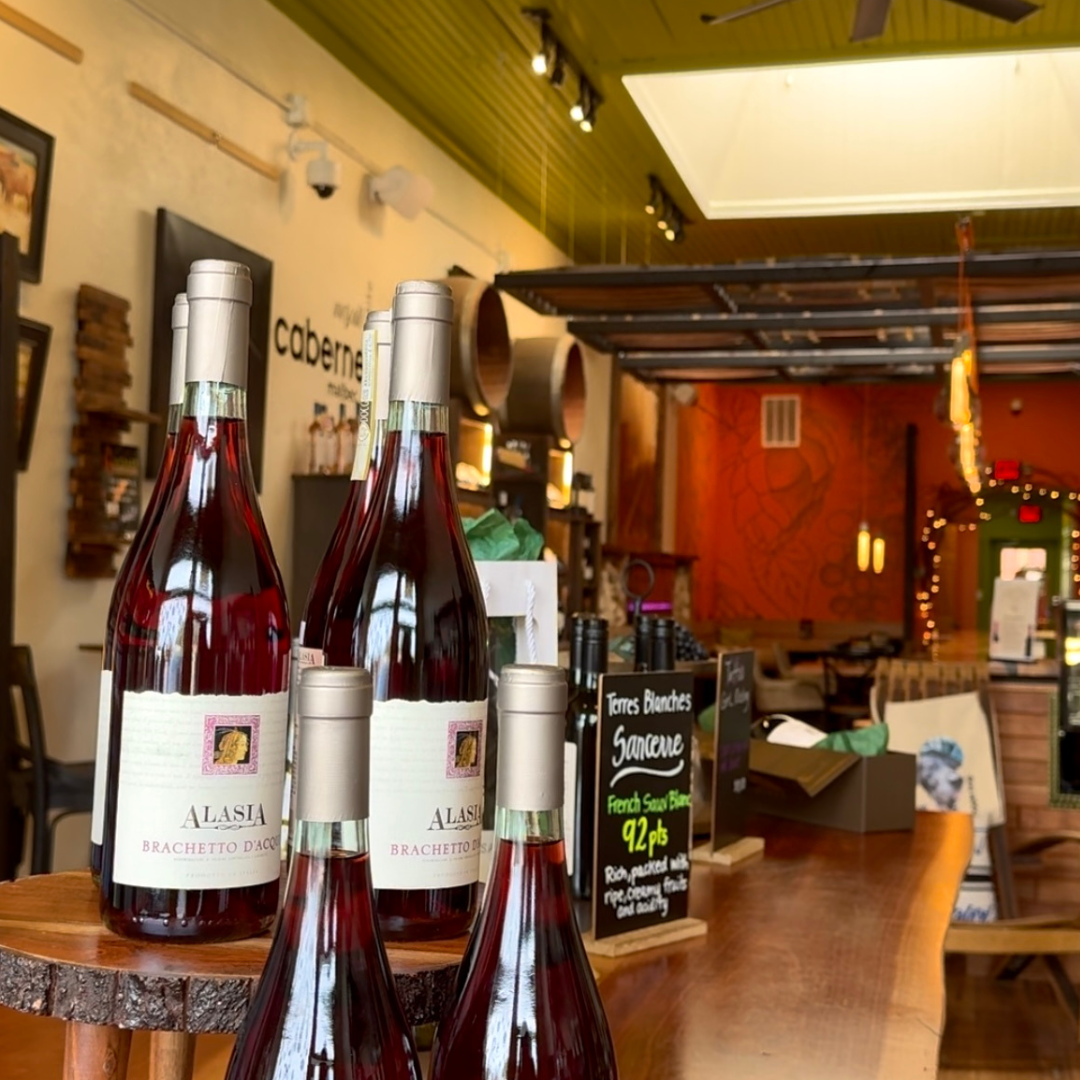 Bottles of Alasia Brachetto d'Acqui wine sit elegantly on a wooden table in a charming wine shop, featuring shelves, decorative items, and a green ceiling. It's just one of the five new reasons to put Acworth on your travel bucket list.