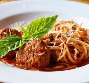 A white plate with spaghetti and tomato sauce, topped with shredded cheese. Two meatballs and a basil leaf are placed beside the pasta—a perfect dish to savor before exploring Acworth's 6 must-visit spots for the perfect Valentine's Day.