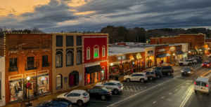 A quaint downtown street in Acworth at dusk, lined with charming shops and parked cars. The cloudy sky overhead sets the perfect scene for exploring, perhaps leading you to discover 6 Winter Combos for Fresh Food + a Good Mood amidst the twinkling lights.