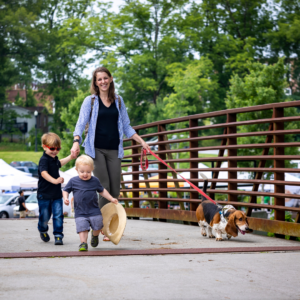 A woman explores Acworth with two young children and a dog on a leash, strolling across a metal bridge. With trees and parked cars in the background, this charming scene gives you just a handful of reasons to put Acworth on your travel bucket list.