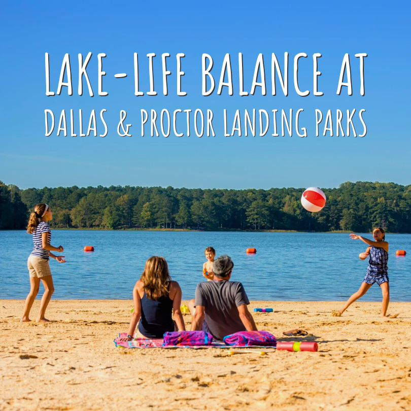 Two people sit on a sandy lakeshore while four others play with a beach ball near the water under a clear blue sky. Text reads: "Lake-life balance at Dallas & Proctor Landing Parks.
