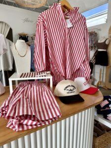 A display of red and white striped shirt and shorts, alongside two baseball caps, arranged on a wooden table at Hippie Kids in Downtown Acworth.
