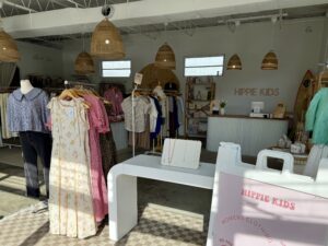 A boutique clothing store with dresses on racks, a mannequin, and a display table with jewelry reflects the story behind Hippie Kids and Cafe de Coco—a creative space highlighted by the "HIPPIE KIDS" sign in the background.