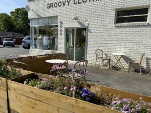 Outdoor seating area with metal chairs and tables in front of "Groovy Clothing" in Downtown Acworth; wooden planters with flowers separate the seating from the street, evoking a chill Hippie Kids Cafe vibe.