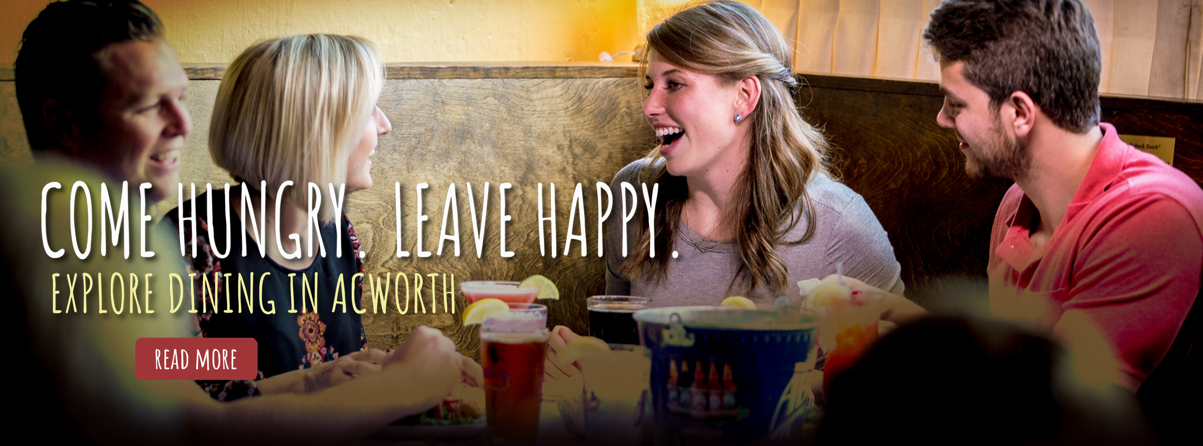 Four people sit at a restaurant table, smiling and talking over drinks and food. Text reads: "Come hungry. Leave happy. Explore dining in Acworth.