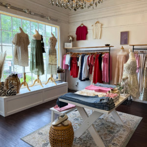 A boutique clothing store perfect for a weekend in Acworth displays dresses on mannequins, folded shirts and pants on tables, and various garments hanging on racks by a large window.
