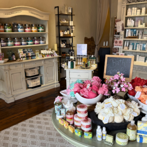 A boutique shop interior displays bath products, soaps, and lotions on tables and shelves, with a "Bath Bombs" chalkboard sign and decorative flowers—perfect for discovering unique finds during a weekend in Acworth.