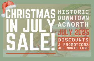 Promotional graphic for "Christmas in July Sale" in Historic Downtown Acworth, July 2025, with discounts and promotions all month long. A Santa hat decorates the text.