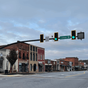 A quiet downtown street with historic buildings, empty sidewalks, and a green traffic light at Lemon Street offers a glimpse into the past. Learn More About Historic Acworth Locations beneath the cloudy sky.