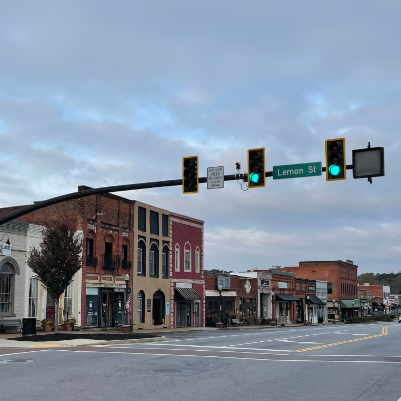 A quiet downtown street with historic buildings, empty sidewalks, and a green traffic light at Lemon Street offers a glimpse into the past. Learn More About Historic Acworth Locations beneath the cloudy sky. A quiet downtown street with historic buildings, empty sidewalks, and a green traffic light at Lemon Street offers a glimpse into the past. Learn More About Historic Acworth Locations beneath the cloudy sky.